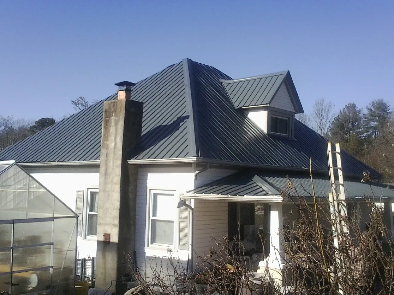Dark blue standing seam metal roof on a white farmhouse with dormer — Slate & Tile Roof Repair by Roofing Brothers in Yellow Spring