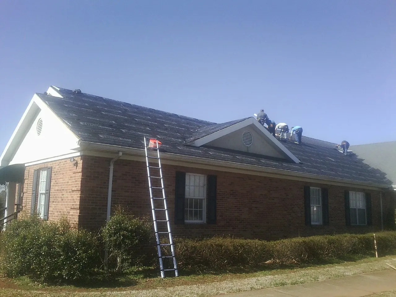 Crew tearing shingles off a brick ranch roof with a ladder set — Emergency Roof Repair work by our crew in Yellow Spring