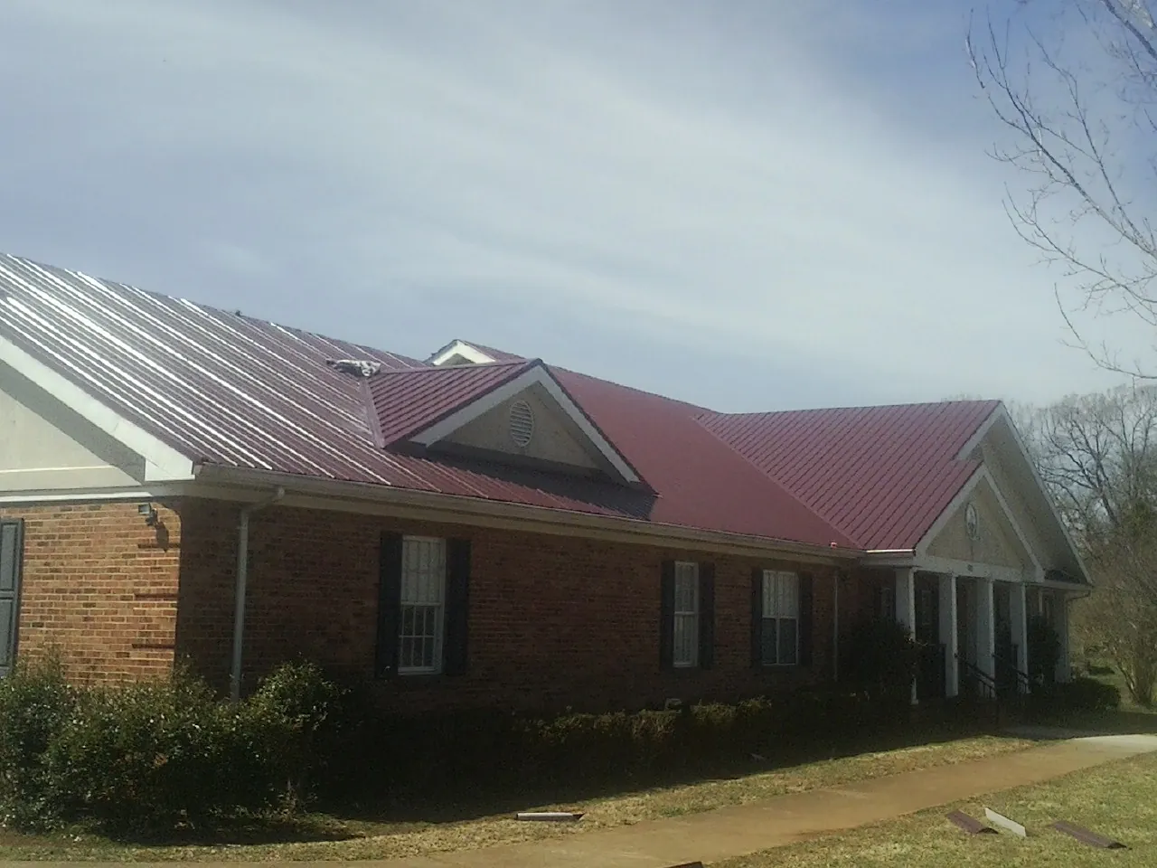Red metal roof with gabled entries on a long brick building, from a Hail Damage Roof Repair job in Yellow Spring