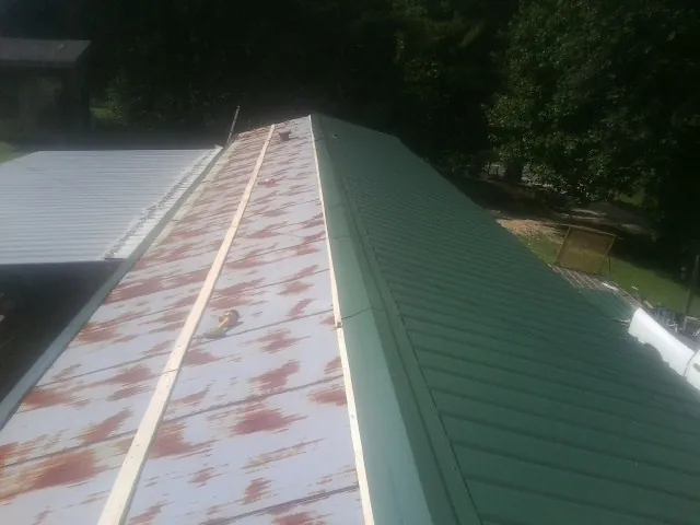 Old rusted panels beside newly installed green metal roofing — Wind Damage Roof Repair by Roofing Brothers in Yellow Spring