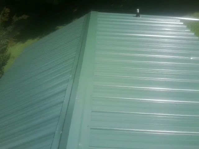 New green metal panels meeting at the ridge of a roof — Flat Roof Repair work by our crew in Yellow Spring