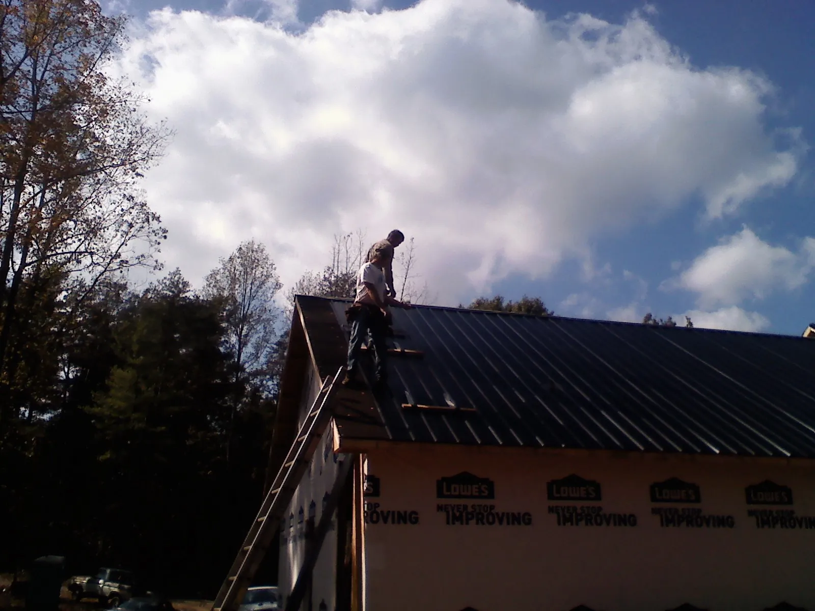 Roofer fastening dark metal panels high against a cloudy sky, from a Roof Inspection job in Yellow Spring