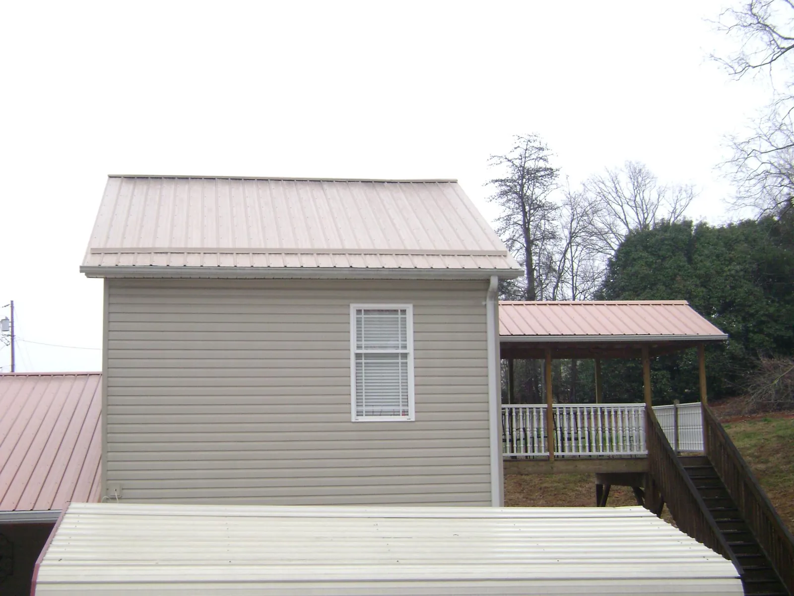 Tan metal roofs on a two story addition and attached porch, from a Roof Replacement job in Yellow Spring